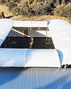 Aerial view of a rectangular outdoor space covered by white fabric canopies with open sides, surrounded by buildings and a dry, grassy landscape. A "Rapid Cover" logo is visible in the bottom right corner.